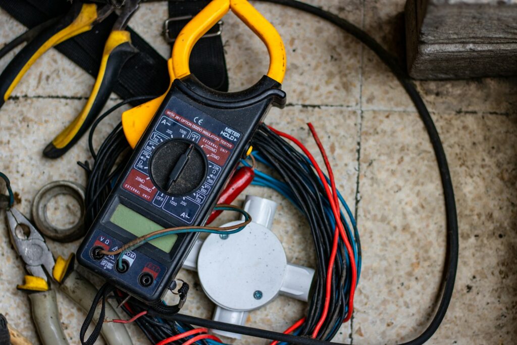Electrician tools including a clamp meter and pliers on a job site floor