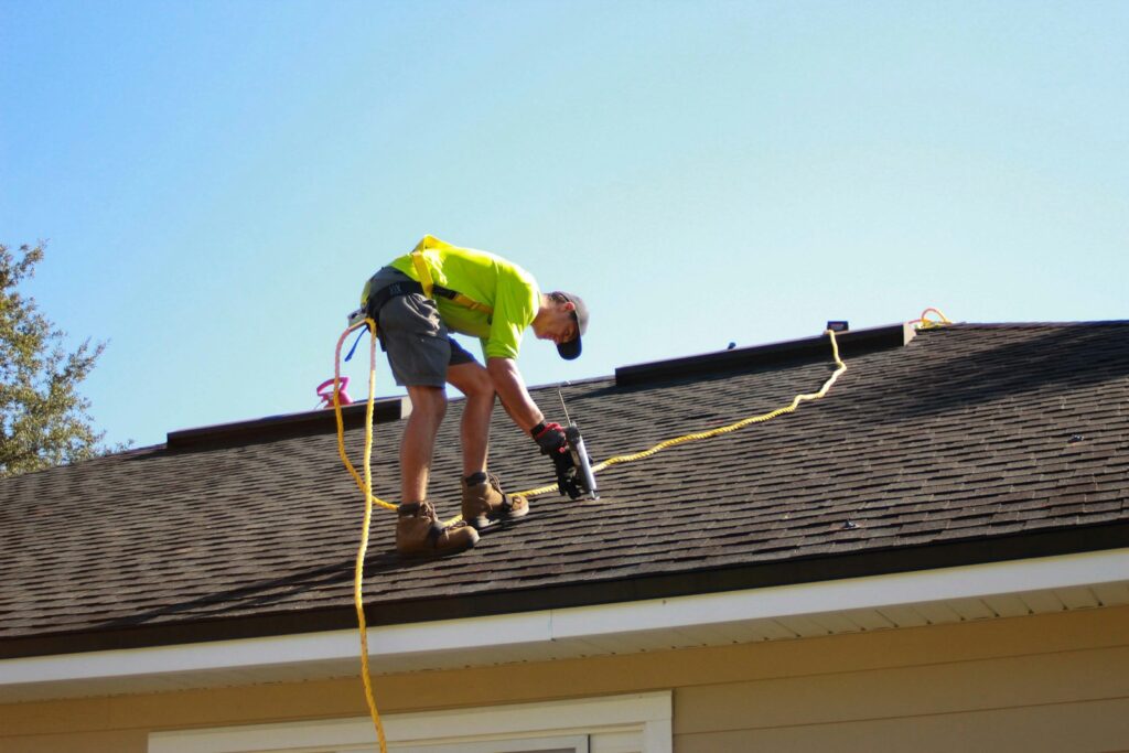 Roofer using a power drill on an asphalt shingle roof - local SEO for roofers