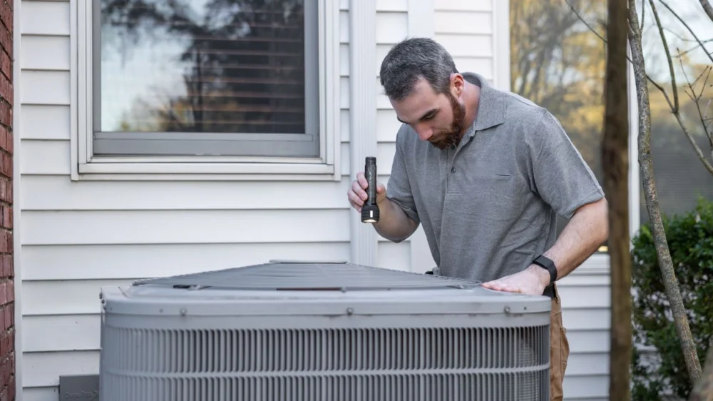 HVAC technician inspecting an outdoor air conditioning unit with a flashlight